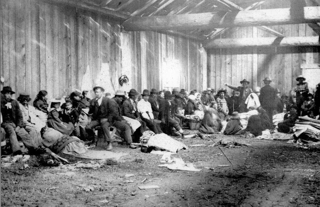 Old photo of people gathered in a large wooden building.