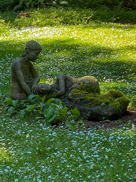 Life-sized sandstone sculpture of two people on the grass.  One is sitting and the other is lying with her head in his lap.