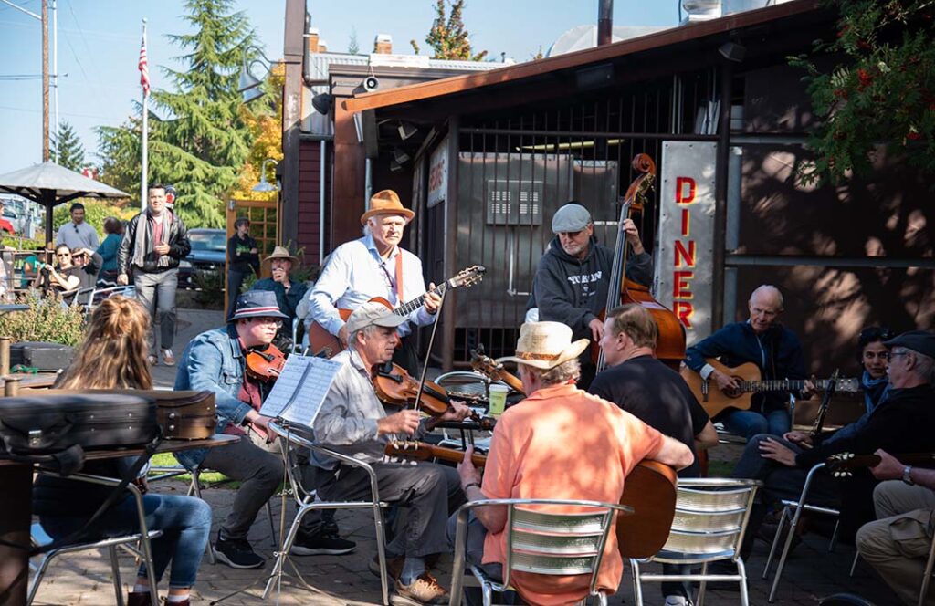 Musicians gathered around an outdoor table playing music.