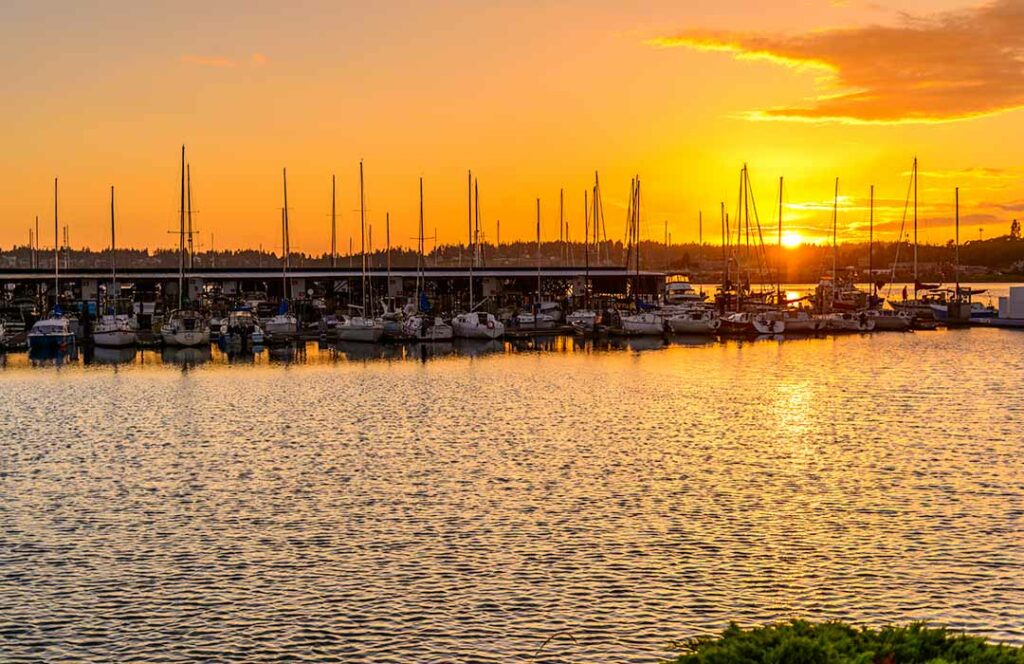 The sun is setting behind boats moored at a marina.