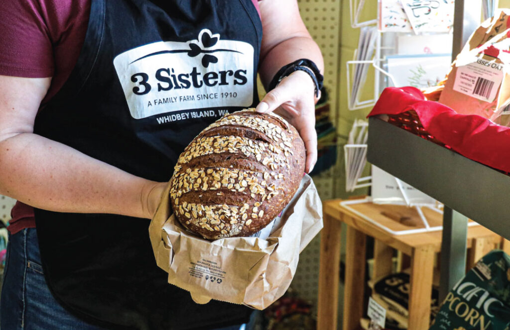 Roshell at Three Sisters Market holds a loaf of fresh bread by Little Red Hen Bakery