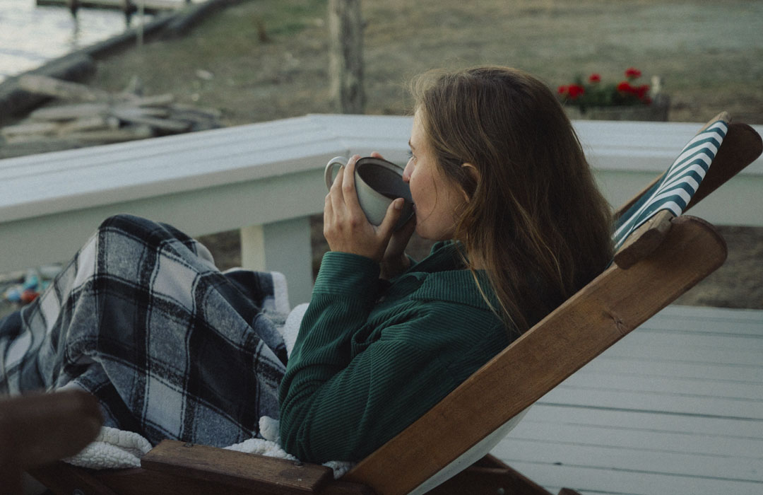 Woman sips coffee on beach house deck, gazing out at Saratoga Passage