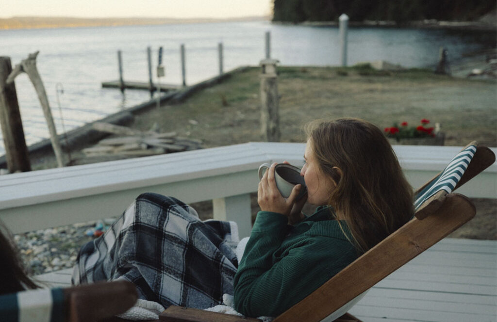Woman sips coffee on beach house deck, gazing out at Saratoga Passage