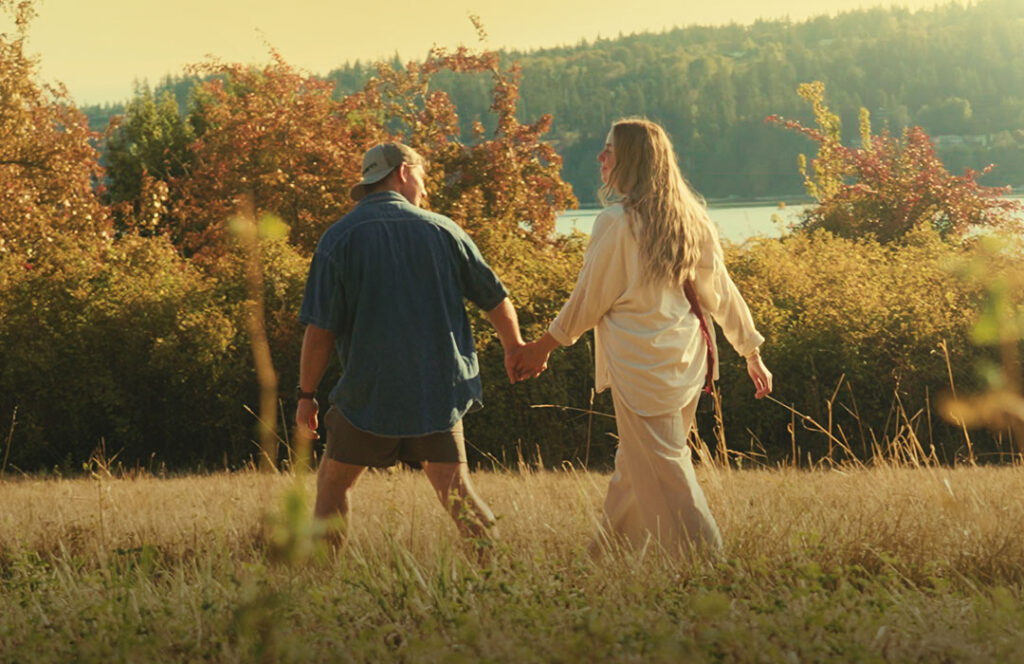 Man and woman walk through field at sunrise